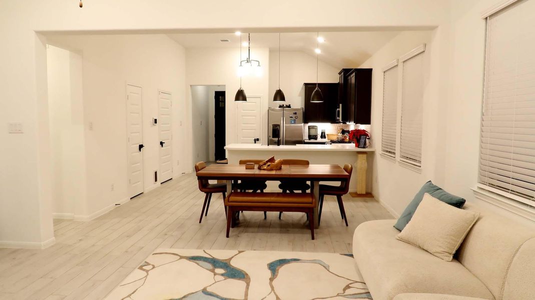 This inviting open-concept living area features a modern kitchen . Adjacent is a cozy dining space. The room is bright and airy, thanks to large windows with blinds and light wood flooring, creating a warm, welcoming atmosphere. This inviting open-concept living area features a modern kitchen . Adjacent is a cozy dining space. The room is bright and airy, thanks to large windows with blinds and light wood flooring, creating a warm, welcoming atmosphere.