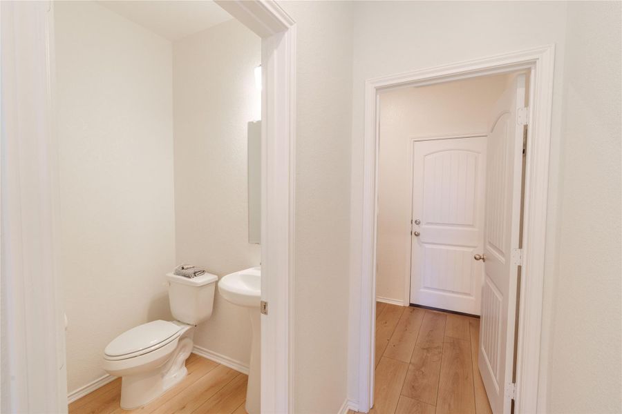 A well-lit powder room features a pedestal sink and modern toilet with natural wood flooring. A well-lit powder room features a pedestal sink and modern toilet with natural wood flooring.