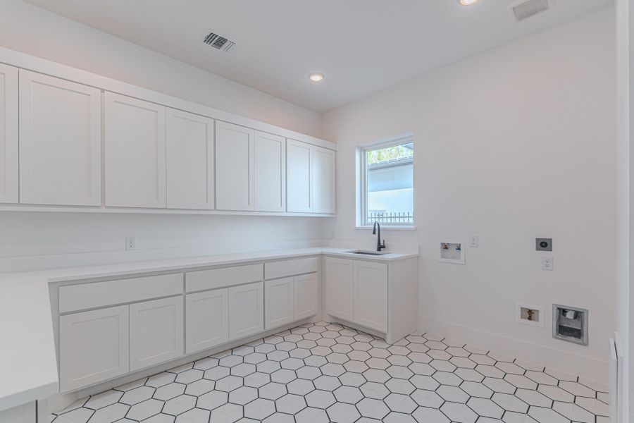 This photo shows a bright, spacious laundry room with white cabinetry, a small window for natural light, and hexagonal tile flooring. It's equipped with ample storage and hookups for washer and dryer.