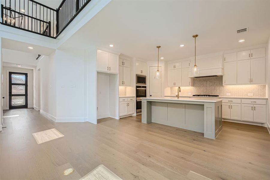 Kitchen with decorative light fixtures, an island with sink, light hardwood / wood-style flooring, and white cabinets