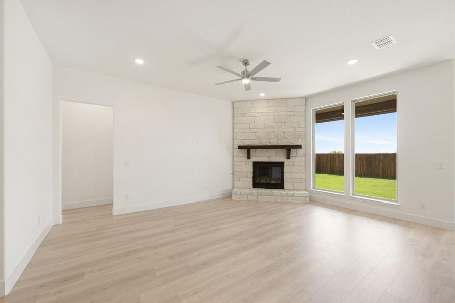 Open living room with stone fireplace, wood mantel, light hardwood floors, and ceiling fan