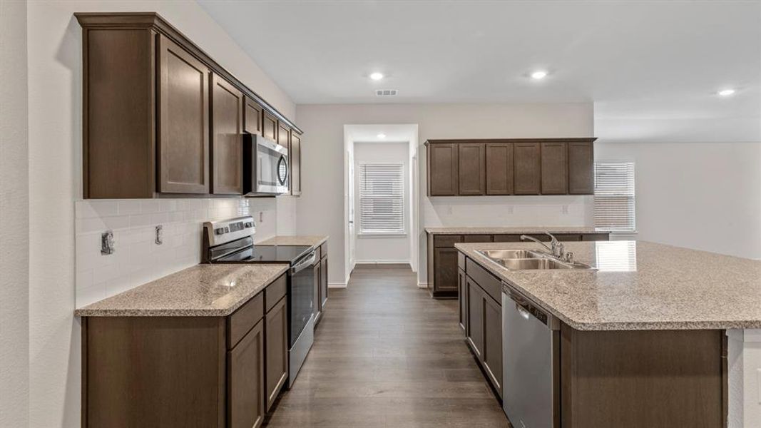 Kitchen featuring dark brown cabinetry, stainless steel appliances, a center island with sink, light stone countertops, and recessed lighting