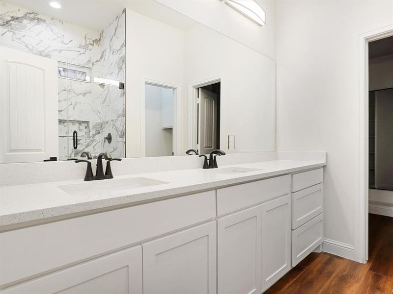 Full bath featuring a marble finish shower, double vanity, and dark wood-style flooring Full bath featuring a marble finish shower, double vanity, and dark wood-style flooring