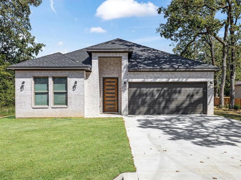 View of front facade featuring concrete driveway, roof with shingles, brick siding, a garage, and a front yard