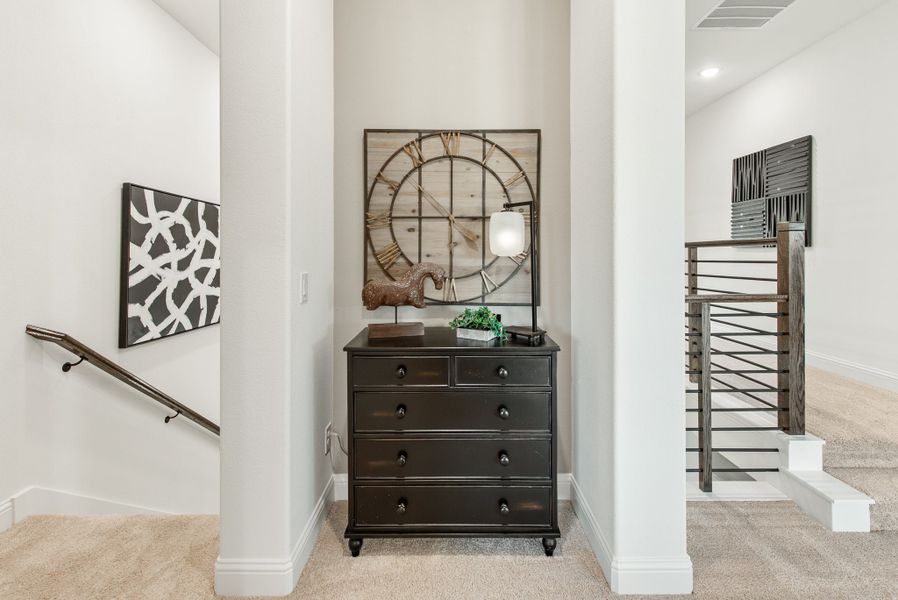 Upstairs hallway landing with dark wood dresser, large wall clock, and metal stair railing on carpet flooring
