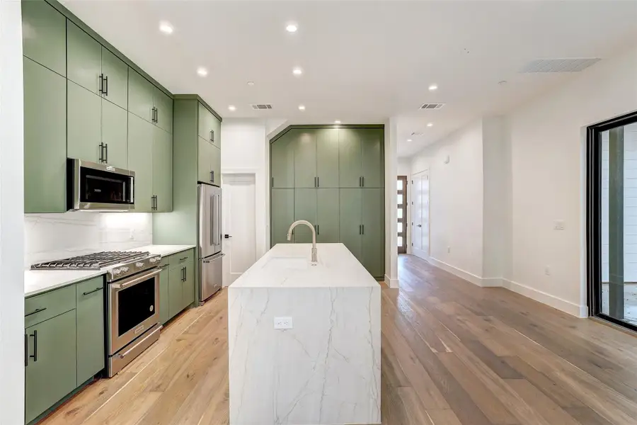 Kitchen with green cabinetry, stainless steel appliances, a sink, light wood finished floors, and recessed lighting