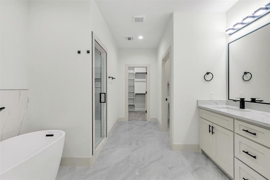 Bathroom with a spacious closet, a freestanding tub, vanity, recessed lighting, and light marble finish flooring