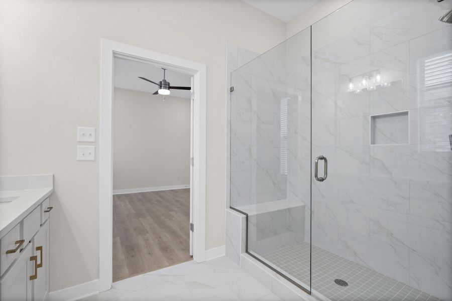 Glass-enclosed shower with a built-in bench and recessed niche, complemented by a vanity featuring a light-toned countertop and gold-finish hardware