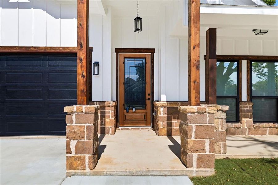 Entrance to property featuring covered porch, a garage, board and batten siding, and stone siding