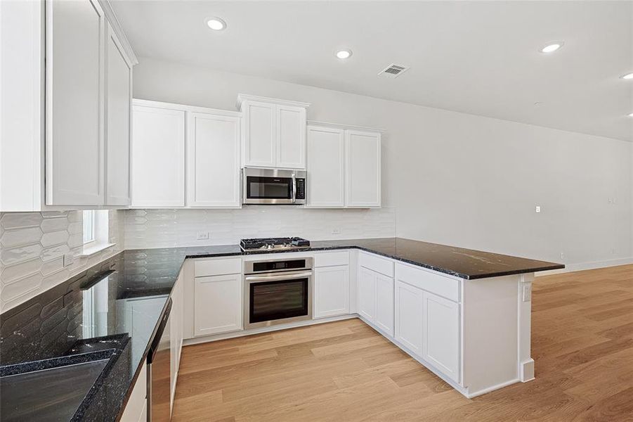 Kitchen featuring light hardwood / wood-style floors, white cabinetry, stainless steel appliances, and dark stone countertops Kitchen featuring light hardwood / wood-style floors, white cabinetry, stainless steel appliances, and dark stone countertops