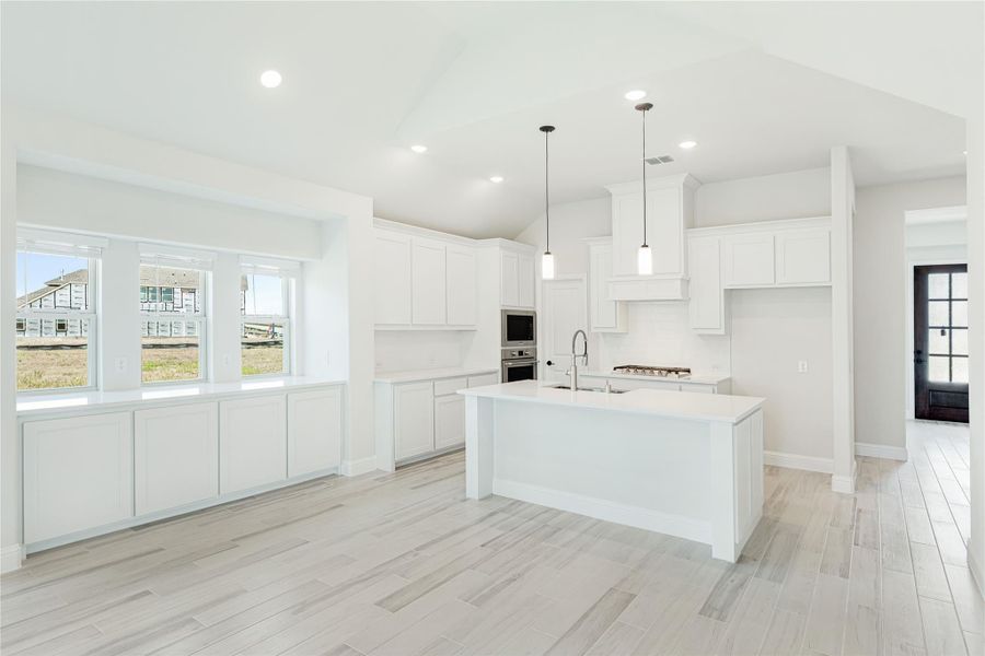 Open kitchen with white cabinets, large center island, pendant lights, and light wood-look tile floors