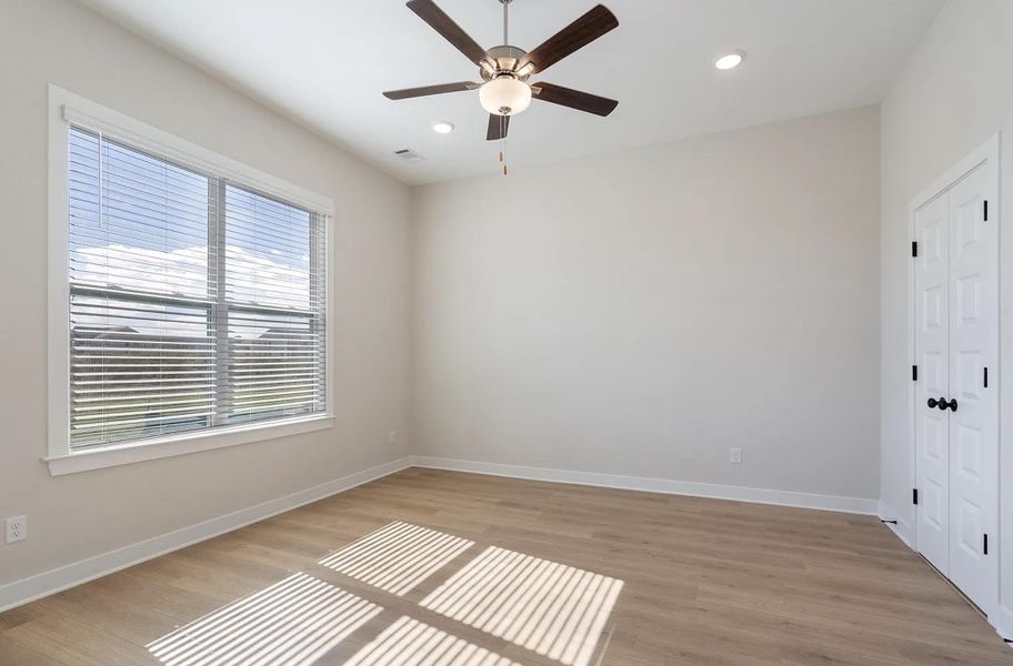 Spacious room featuring light wood-finish flooring, a large window with blinds, recessed lighting, a ceiling fan, and bi-fold closet doors