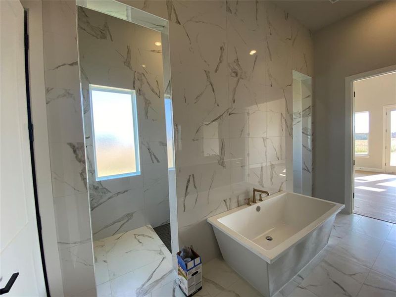 Bathroom with marble tiled flooring, a freestanding bath, a marble finish shower, and stone wall