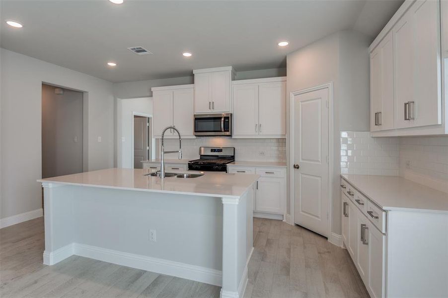 Kitchen featuring a large central island, white cabinetry, integrated stainless steel appliances, a subway tile backsplash, and light wood-finish flooring