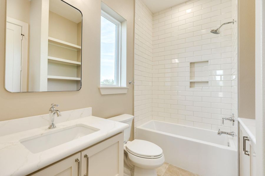 This bathroom features a clean, modern design with white subway tile in the shower, a built-in shelf, and a sleek vanity with a marble countertop. Natural light streams through the window, enhancing the bright, airy feel.