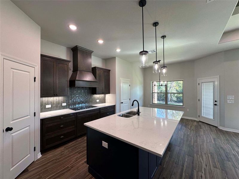 Kitchen featuring a kitchen island with sink, light stone countertops, dark wood-type flooring, decorative light fixtures, and recessed lighting Kitchen featuring a kitchen island with sink, light stone countertops, dark wood-type flooring, decorative light fixtures, and recessed lighting