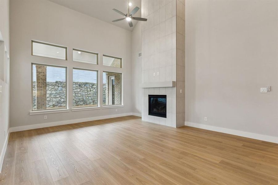 Unfurnished living room featuring light wood-type flooring, ceiling fan, a tile fireplace, and a towering ceiling