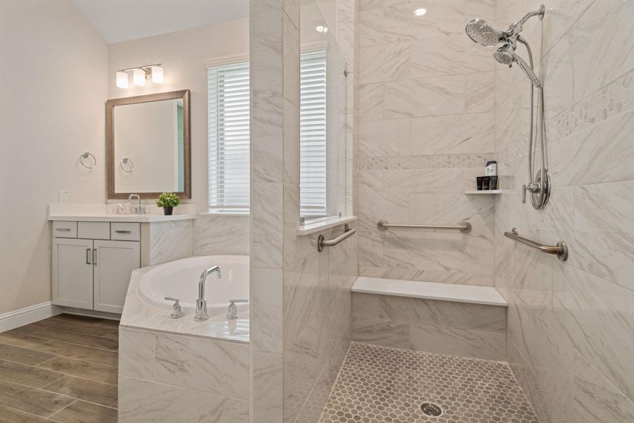 This modern bathroom features a spacious ADA accessible walk-in shower with grab bars and a bench, a soaking tub, and a sleek vanity with ample lighting. The neutral tile and wood-look flooring add a touch of elegance. This modern bathroom features a spacious ADA accessible walk-in shower with grab bars and a bench, a soaking tub, and a sleek vanity with ample lighting. The neutral tile and wood-look flooring add a touch of elegance.