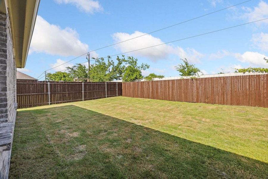 Expansive backyard featuring a manicured lawn, a full wood privacy fence, and a brick exterior wall Expansive backyard featuring a manicured lawn, a full wood privacy fence, and a brick exterior wall