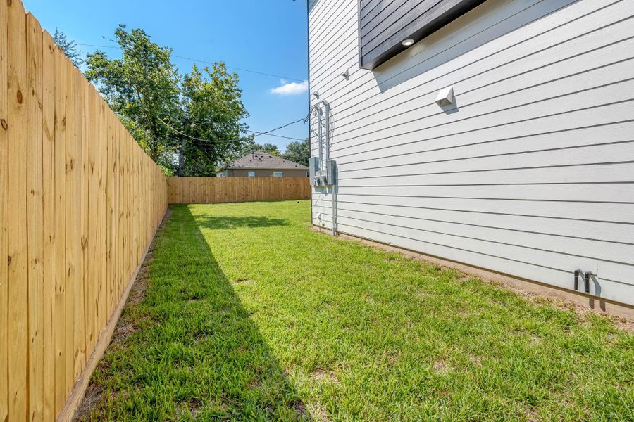 View from the backyard gate looking into the fully fenced yard, showcasing the long stretch of green space along the side of the home and convenient access into the backyard.