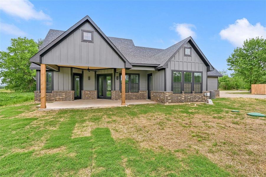Rear view of property with a shingled roof, brick siding, board and batten siding, a patio area, and a lawn