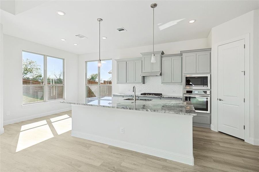 Kitchen with stainless steel appliances, pendant lighting, light hardwood / wood-style floors, gray cabinetry, and light stone counters