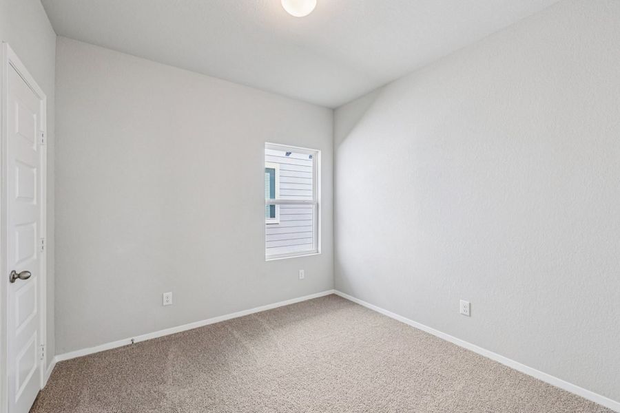 Image of a secondary bedroom with beige walls, tan carpeting and a window