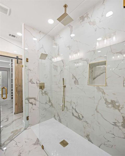 Glass-enclosed shower with full-height marbled wall tiling, square rain shower head, hand-held shower fixture, built-in niche, and gold-toned hardware