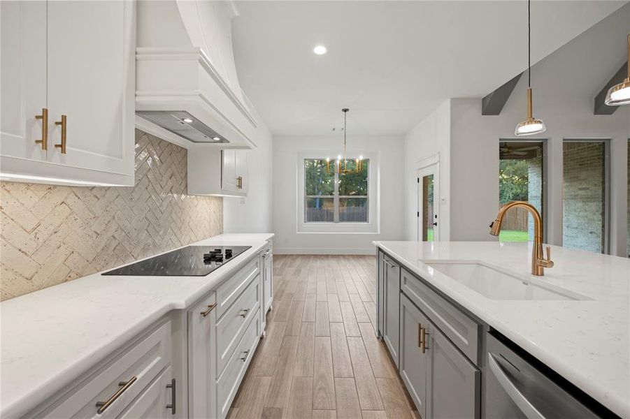 Kitchen featuring light stone counters, white cabinetry, backsplash, pendant lighting, and light wood finished floors