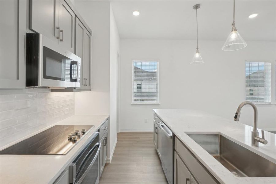 Kitchen featuring gray cabinetry, sink, tasteful backsplash, decorative light fixtures, and appliances with stainless steel finishes