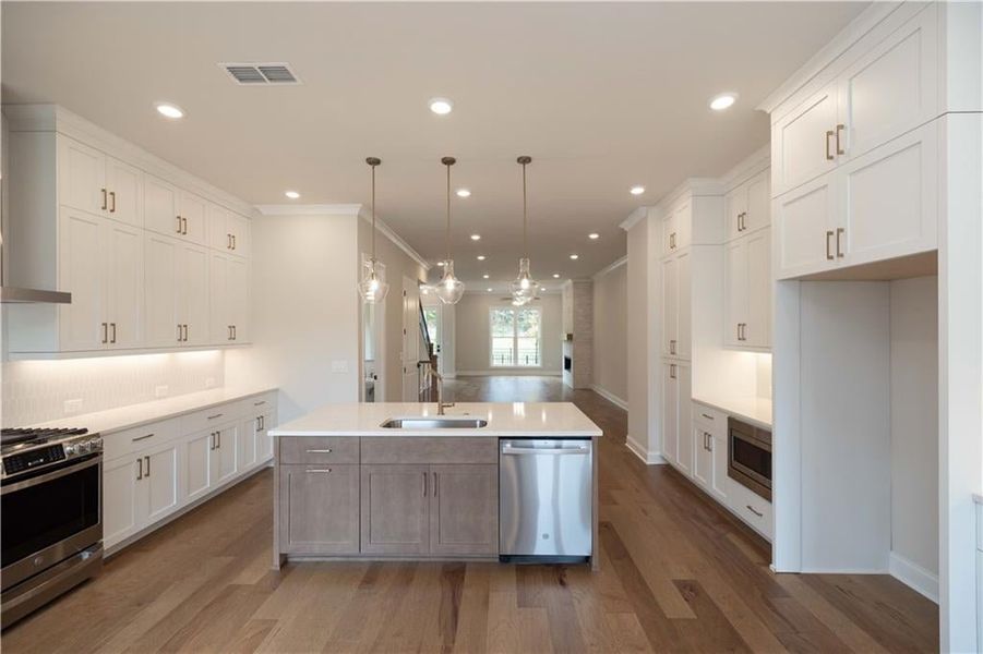 Kitchen with stainless steel appliances, hanging light fixtures, a kitchen island with sink, and sink