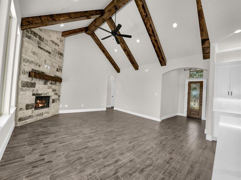 Unfurnished living room featuring high vaulted ceiling, a stone fireplace, beamed ceiling, arched walkways, and dark wood finished floors