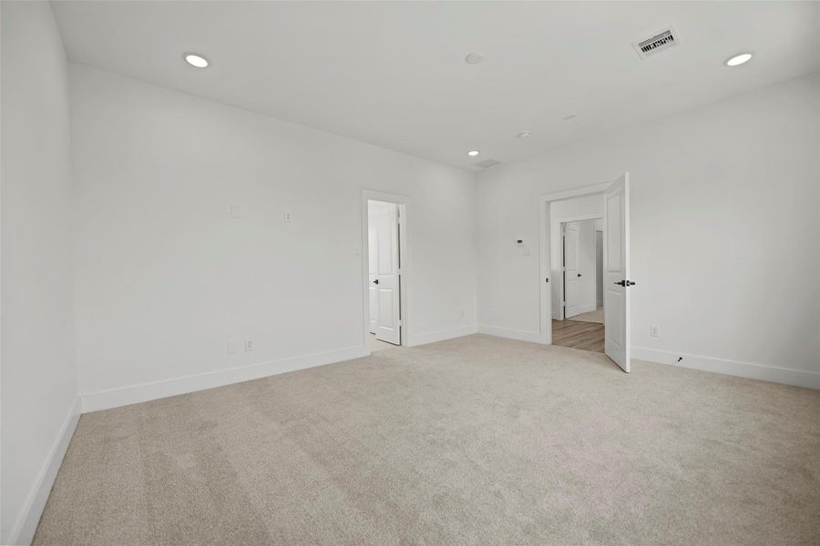 This primary bedroom is bright, spacious and has neutral carpet and walls, featuring recessed lighting and a door leading to the walk-in closet and another door leading to adjoining the primary bathroom.