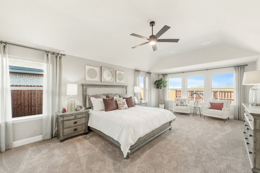 Spacious master bedroom with vaulted ceiling, ceiling fan, carpet flooring, and large windows with natural light