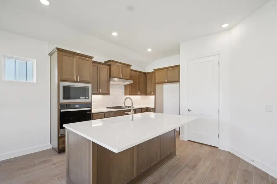 Kitchen with vaulted ceiling, light wood finished floors, a kitchen island with sink, stainless steel appliances, and tasteful backsplash