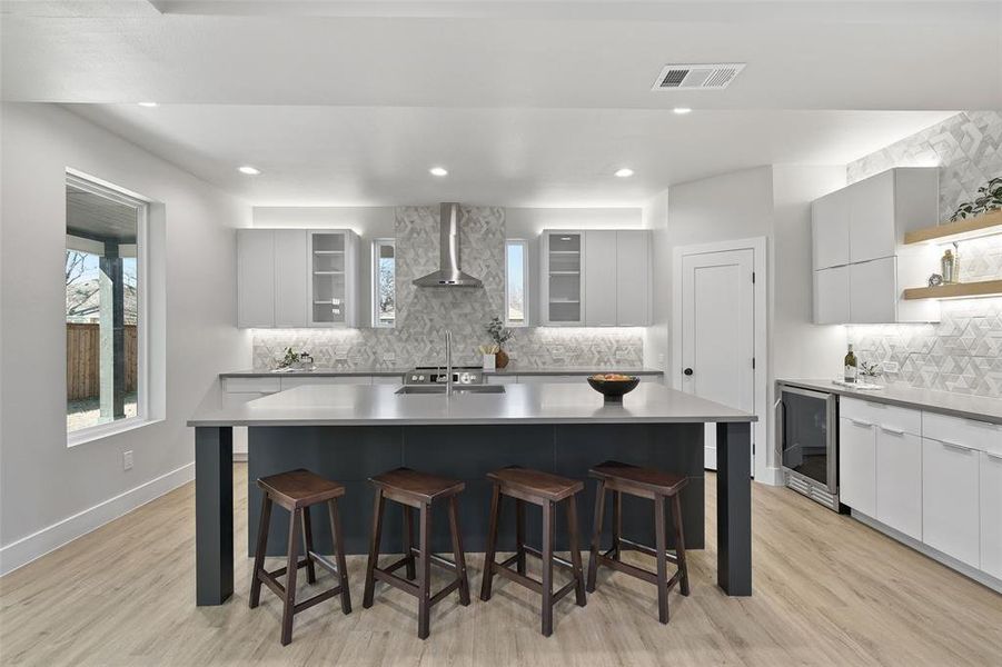 Kitchen featuring a breakfast bar, beverage cooler, wall chimney exhaust hood, and an island with sink