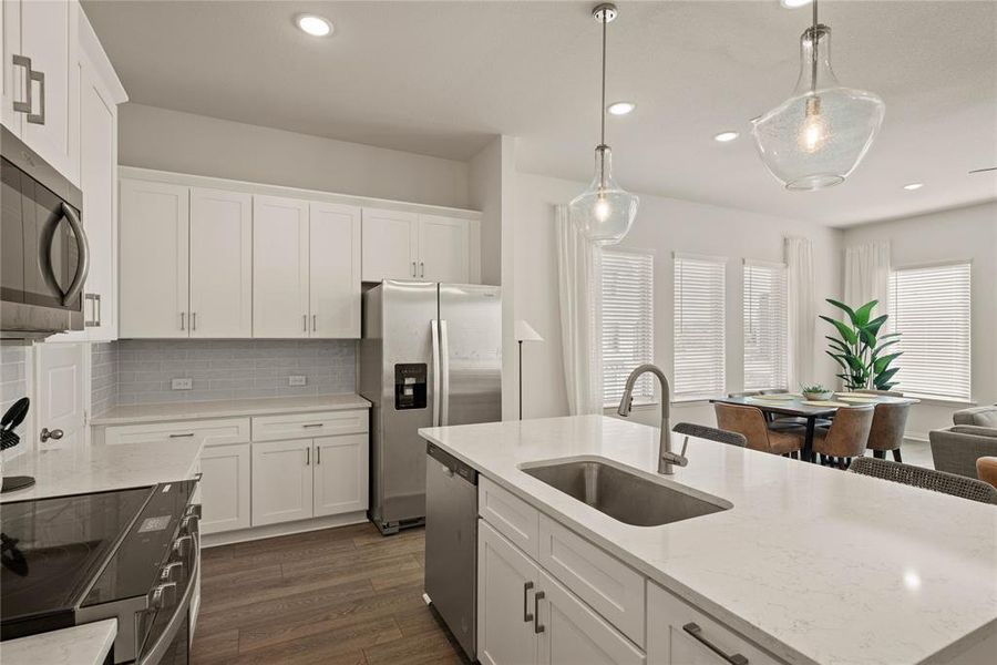 Kitchen featuring decorative light fixtures, sink, white cabinets, a kitchen island with sink, and stainless steel appliances