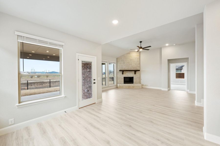 Open living room with light wood floors, stone fireplace, ceiling fan, and patio door access Open living room with light wood floors, stone fireplace, ceiling fan, and patio door access