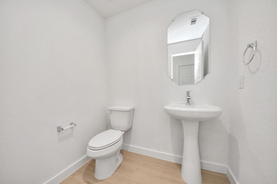This half bathroom features a stylish pedestal sink, modern hardware, and bright recessed lighting, creating a sleek and inviting space. Sample photo of completed home with similar floor plan. Actual colors and selections may vary.