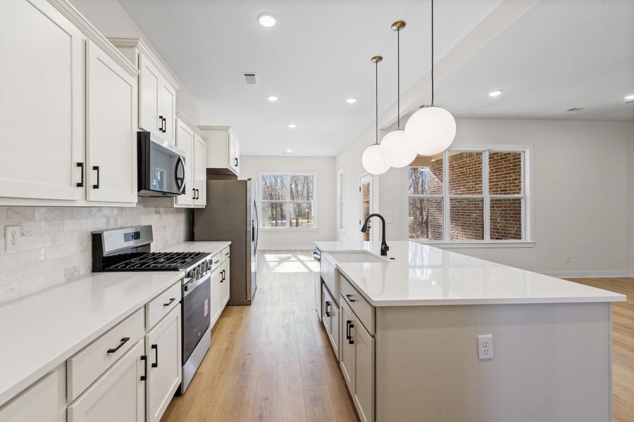 Kitchen featuring stainless steel appliances, light wood-type flooring, pendant lighting, and a center island with sink Kitchen featuring stainless steel appliances, light wood-type flooring, pendant lighting, and a center island with sink