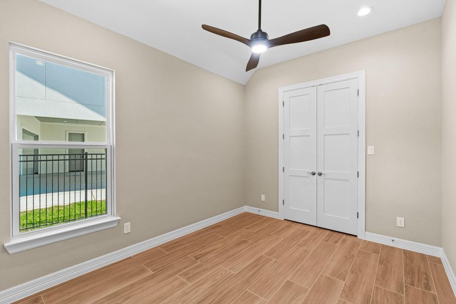 Bright and inviting secondary bedroom with a ceiling fan, large windows, and neutral finishes.