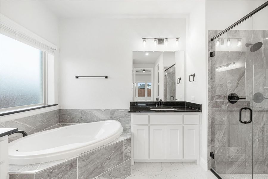 Master bathroom with soaking tub, glass walk-in shower, white vanity, and gray tile surround