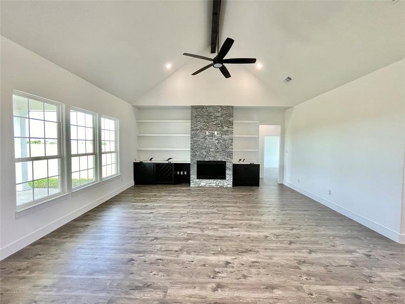 Unfurnished living room featuring wood finished floors, built in shelves, ceiling fan, baseboards, and beam ceiling Unfurnished living room featuring wood finished floors, built in shelves, ceiling fan, baseboards, and beam ceiling