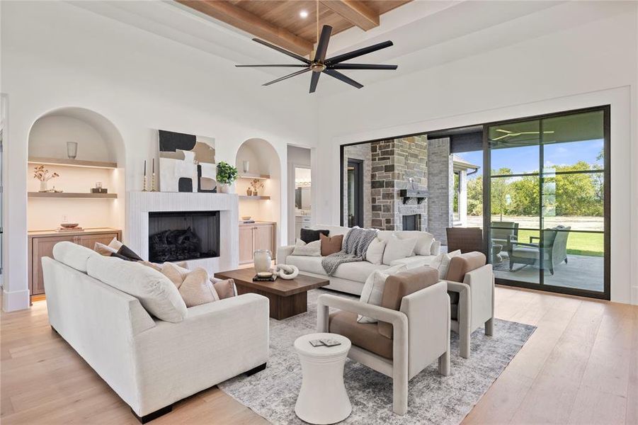 Living area featuring a fireplace, built in shelves, light wood finished floors, a towering ceiling, and ceiling fan