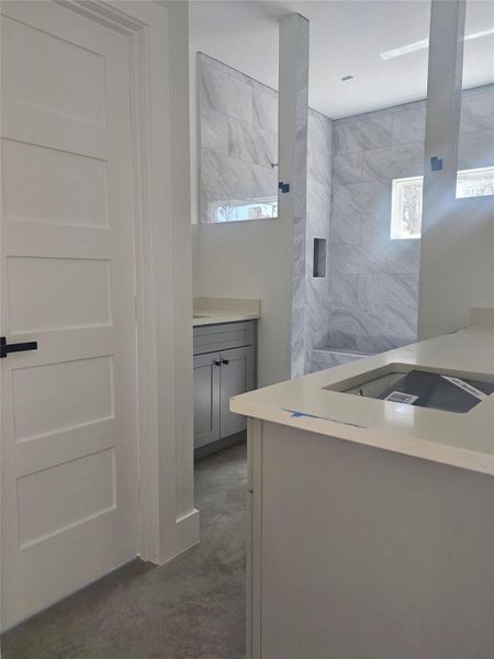 Full bathroom with tiled shower, vanity, and concrete flooring