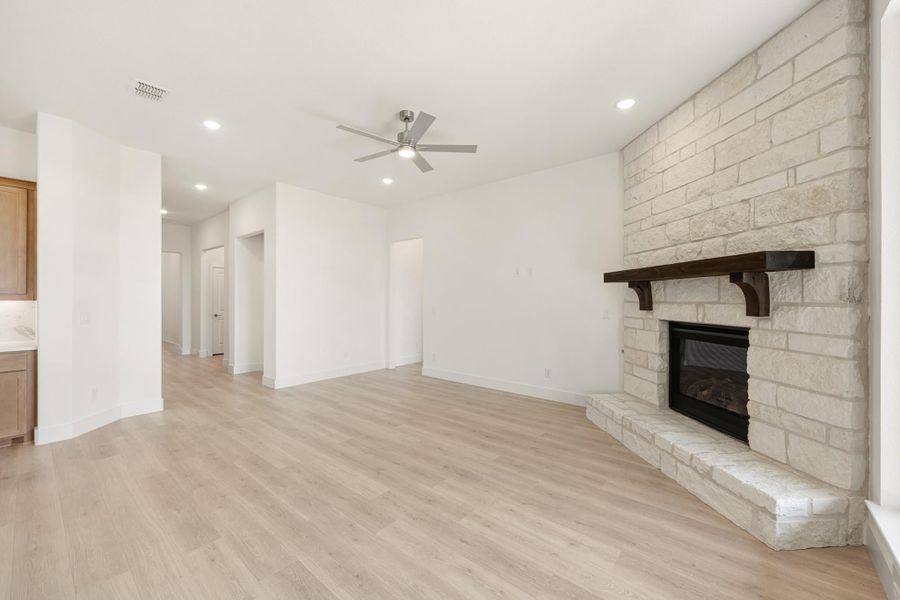 Open living room with light wood floors, ceiling fan, and floor-to-ceiling stone fireplace with wood mantel