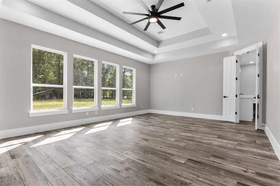Bright primary bedroom featuring large windows with serene views & elegant tray ceiling.