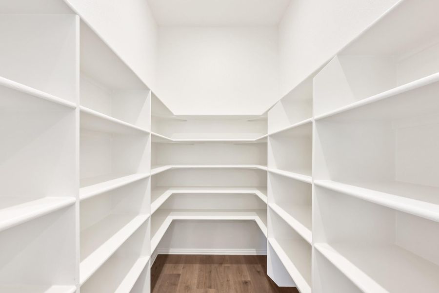 Walk-in pantry with floor-to-ceiling white shelves on three walls and hardwood floors