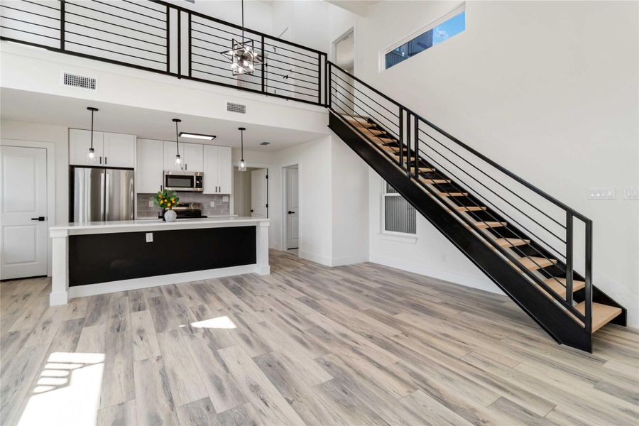 Unfurnished living room featuring a high ceiling, light wood finished floors, and stairway Unfurnished living room featuring a high ceiling, light wood finished floors, and stairway
