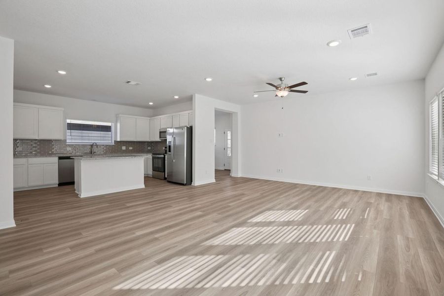 Kitchen with open floor plan, a kitchen island, stainless steel appliances, white cabinets, and light wood finished floors